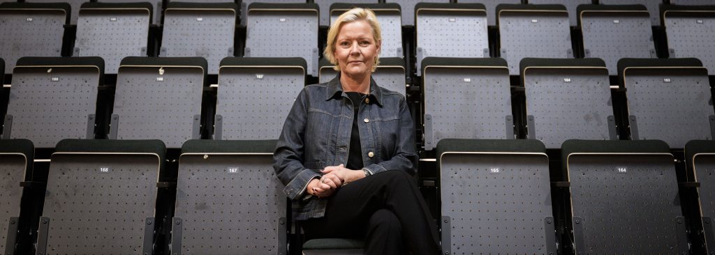 Marie Lindqvist, Senior Vice President Europe på Legends Global, sitter ensam på en numrerad läktare i en tom arena. Hon har armarna i kors och bär en mörk jeansjacka och svarta byxor, med blicken riktad mot kameran.