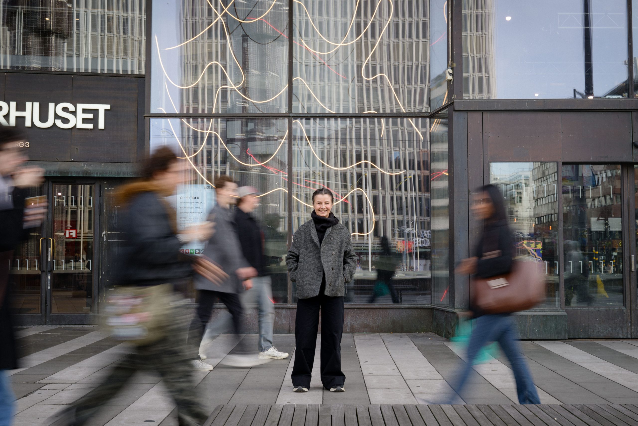Anna Romson, medgrundare av Cogs Creative, sitter utanför Kulturhuset Stadsteatern i Stockholm iklädd en grå jacka och svarta byxor och ler.