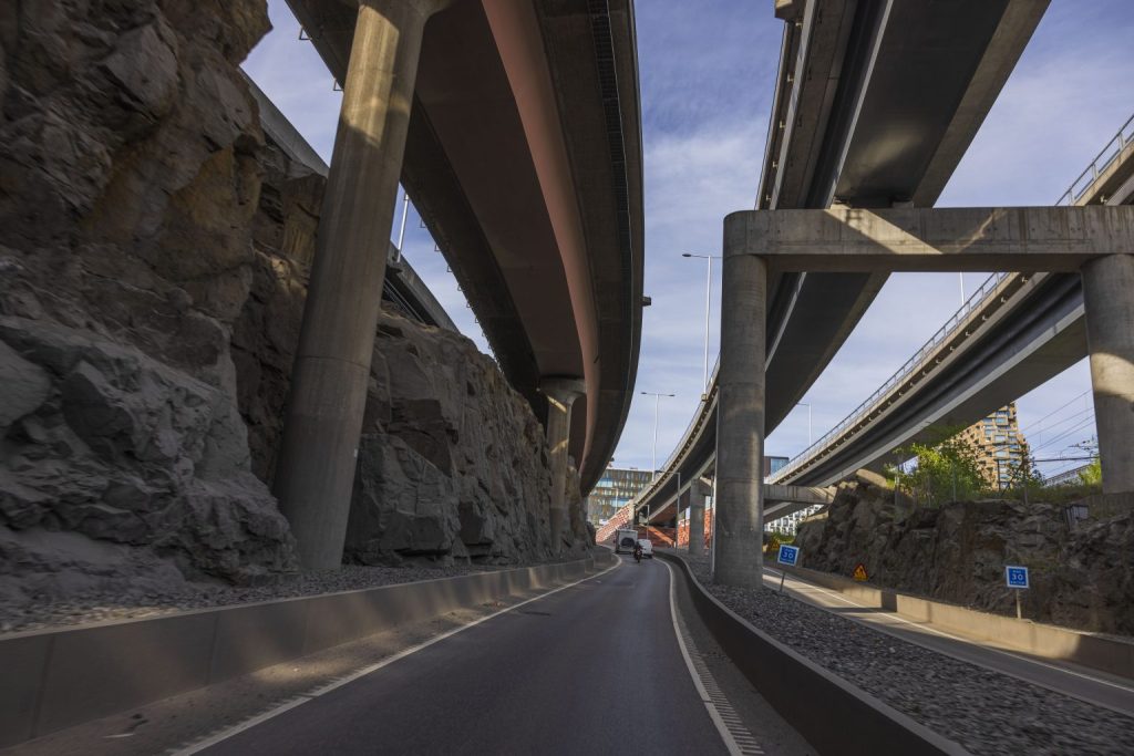 Motorväg som löper under flera broar och viadukter i stadsmiljö med klippor och betongpelare