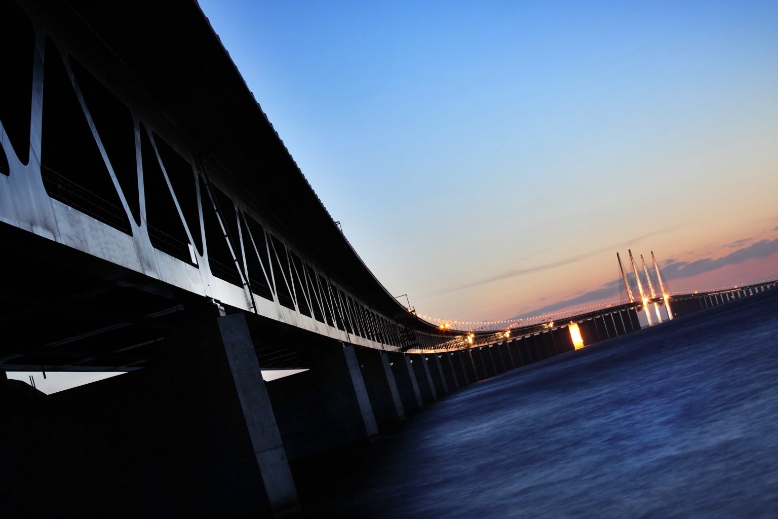 Öresundsbron i skymning över havet, sedd från låg vinkel med brospann och pelare upplysta