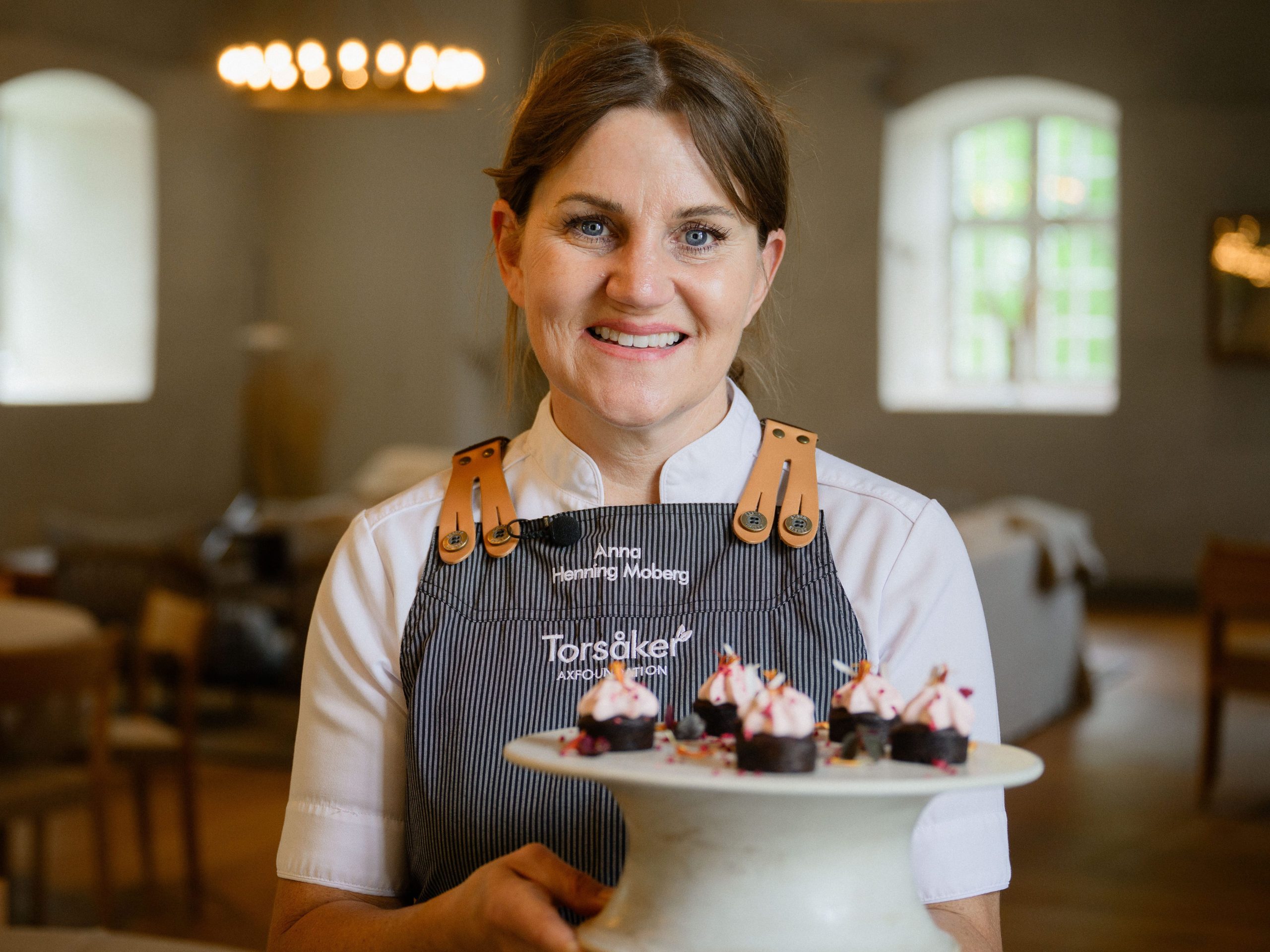 Anna Henning Moberg, verksamhetschef vid Torsåker gård som drivs av Axfoundation, står vid ett fat med brownies toppade med ljusrosa kräm.