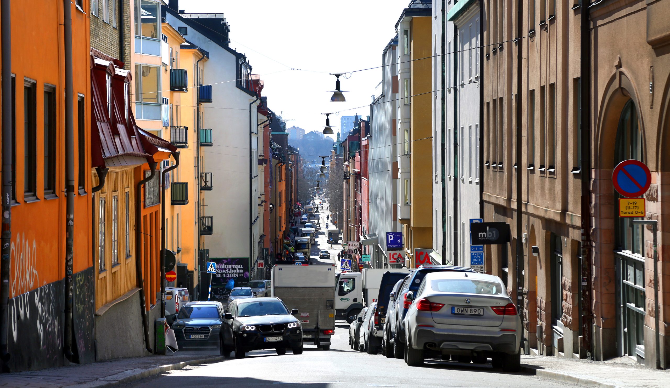 Backig gata i Stockholm med bilar, parkerade fordon och flerbostadshus på båda sidor