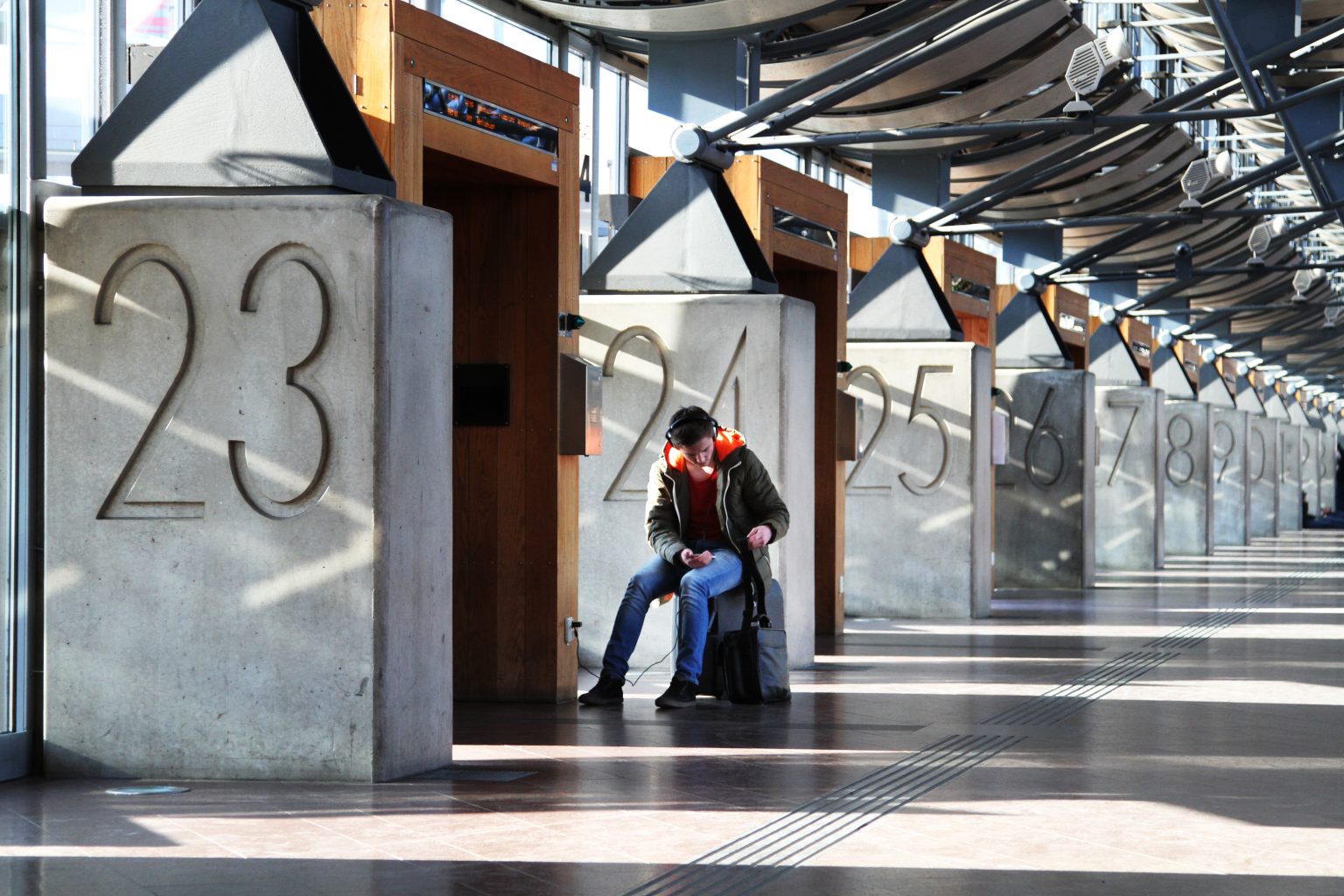 Person sitter i väntsal på tågstation med numrerade portar i modern terminal