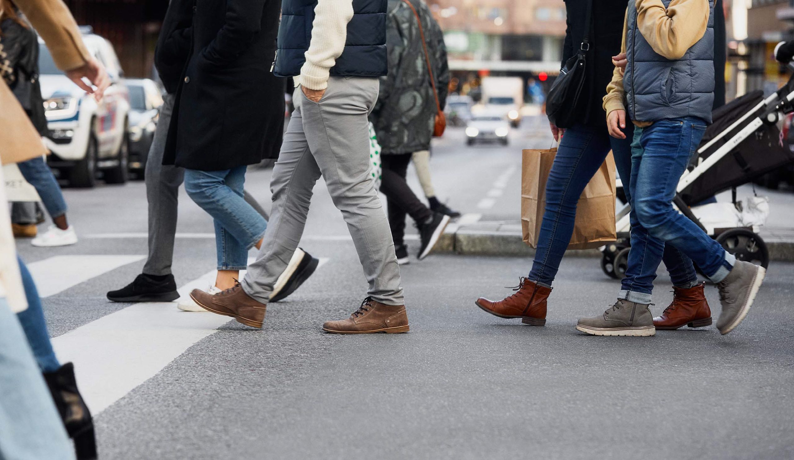 Flera personer som går över ett övergångsställe i stadsmiljö, med bilar och trottoar i bakgrunden