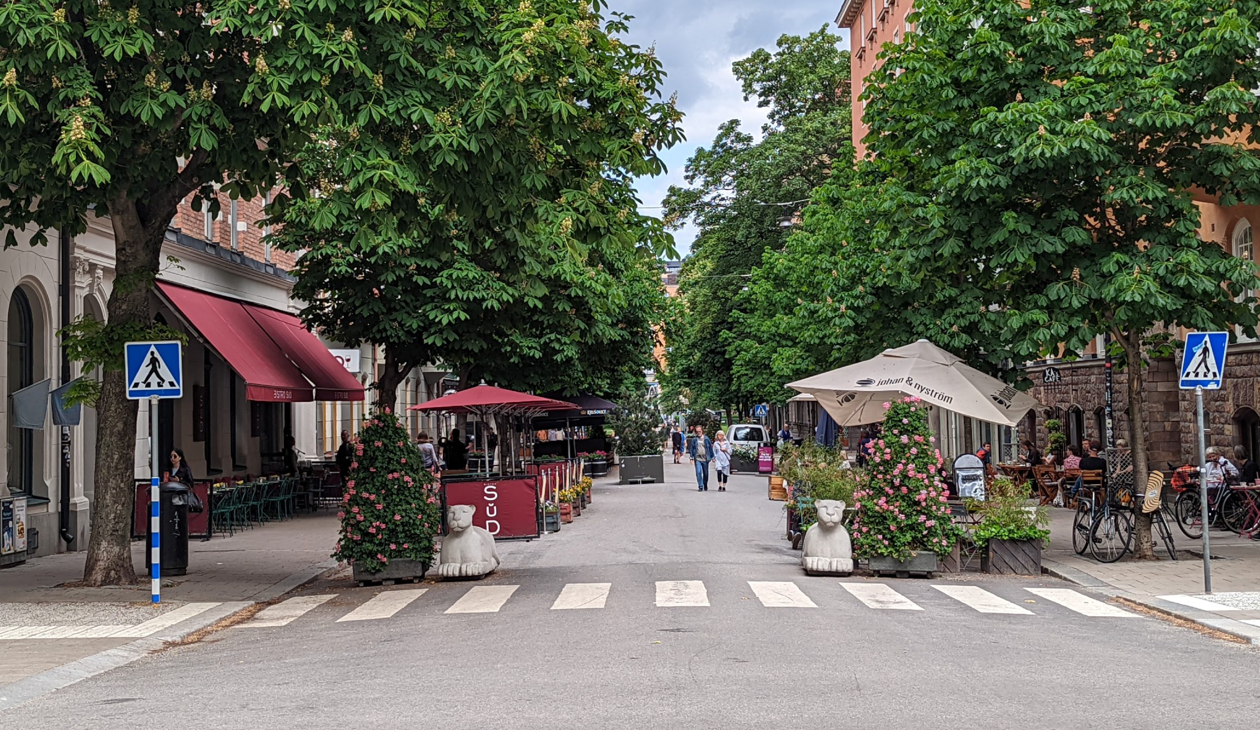 Swedenborgsgatan i Stockholm med uteserveringar, grönska och människor på en bilfri sommargågata