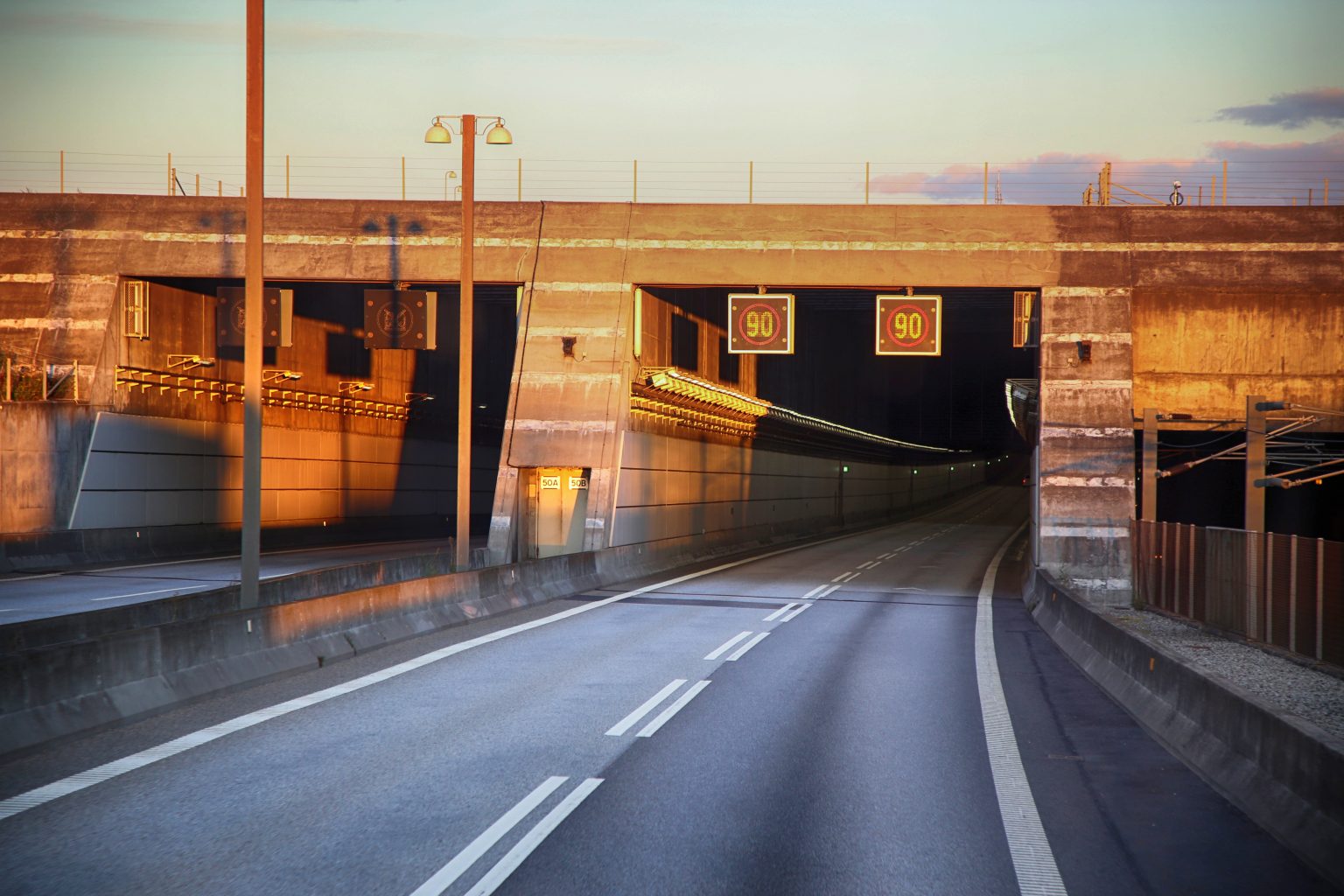 Motorväg som leder in i tunnel med hastighetsskyltar och belysning i kvällsljus