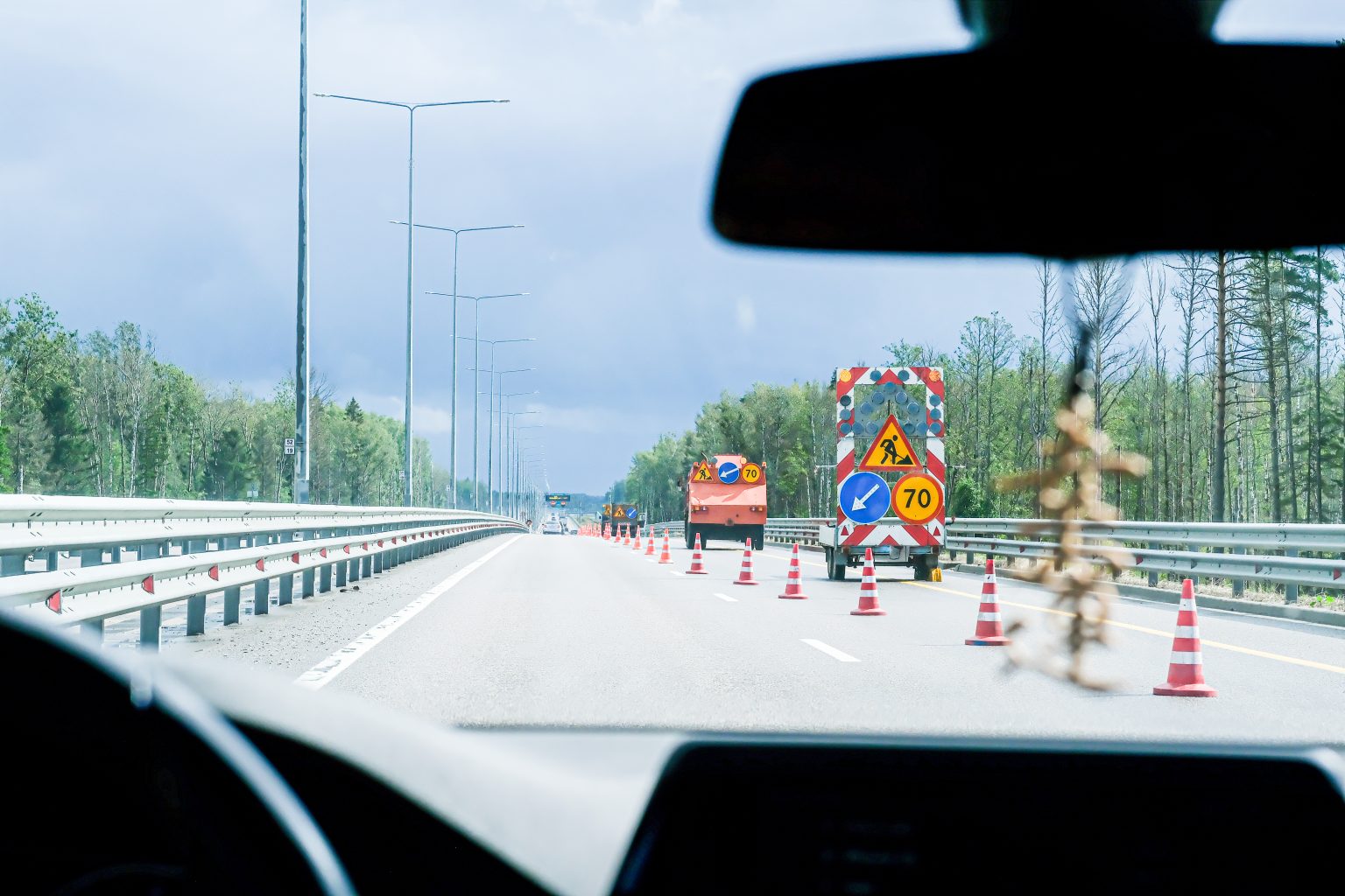 Vägarbete på motorväg med koner, arbetsfordon och sänkt hastighet, sett från bilförarens perspektiv