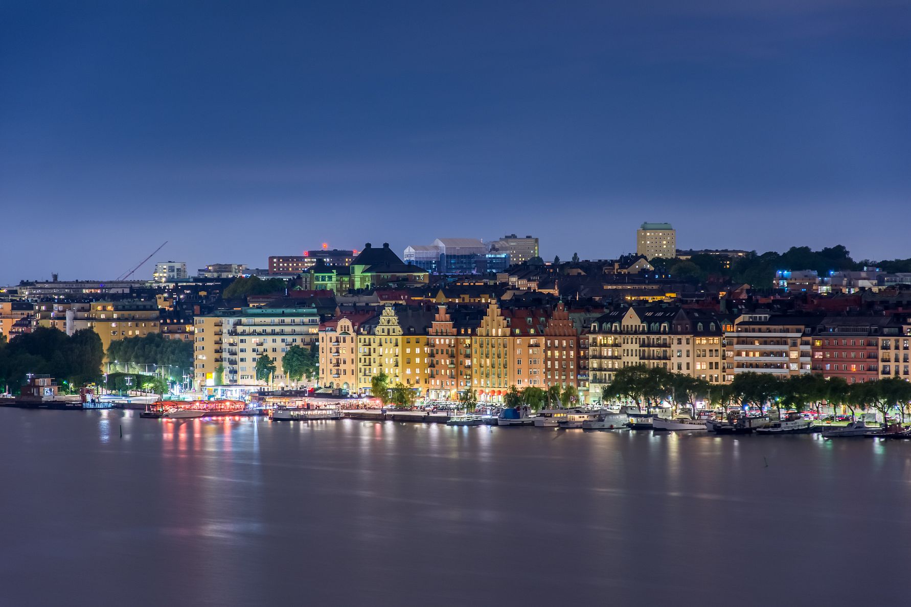 Kvällsbild över Stockholm med upplysta byggnader längs vattnet och stadsliv i fokus, kopplat till Stockholms Handelskammares förslag om Stockholmsnätter och längre öppettider under VM 2026.