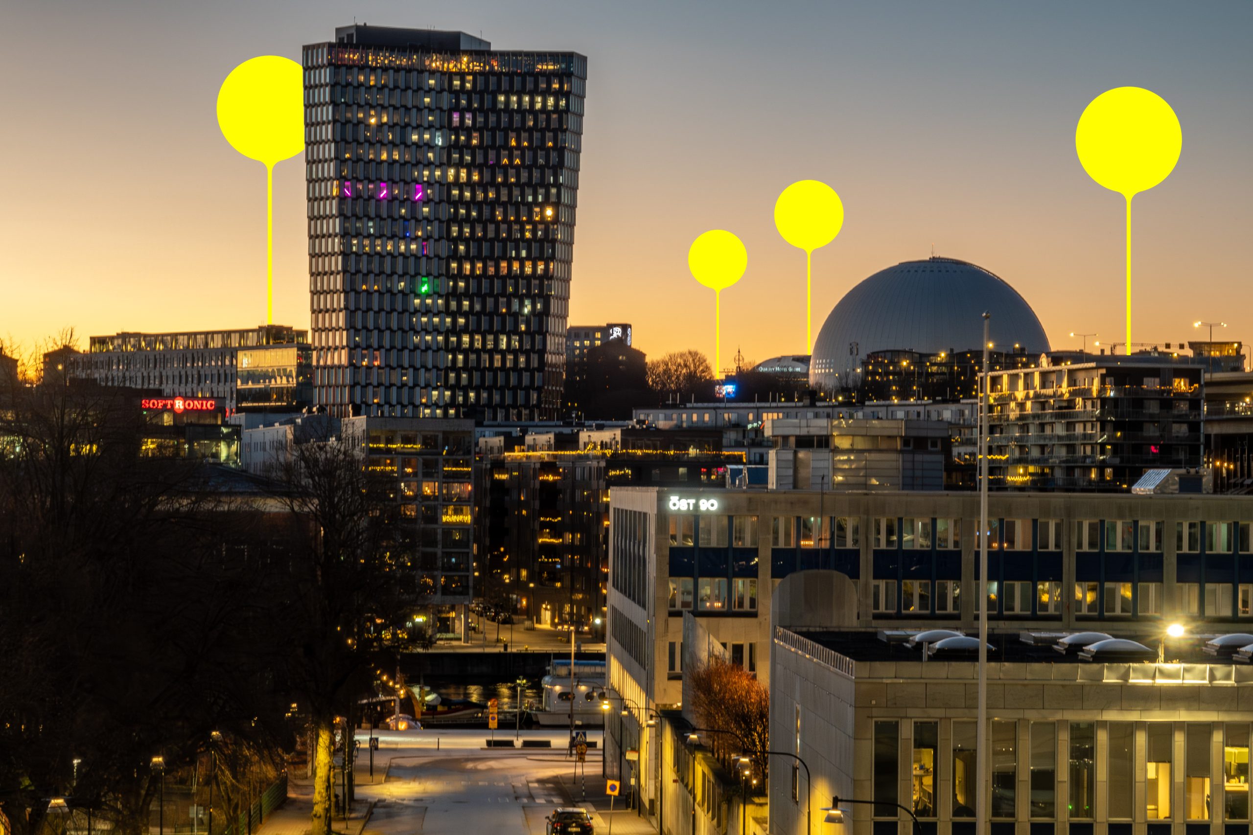 Vy över Stockholm och Globen i skymning, med upplysta kontorsbyggnader och stadsmiljö.