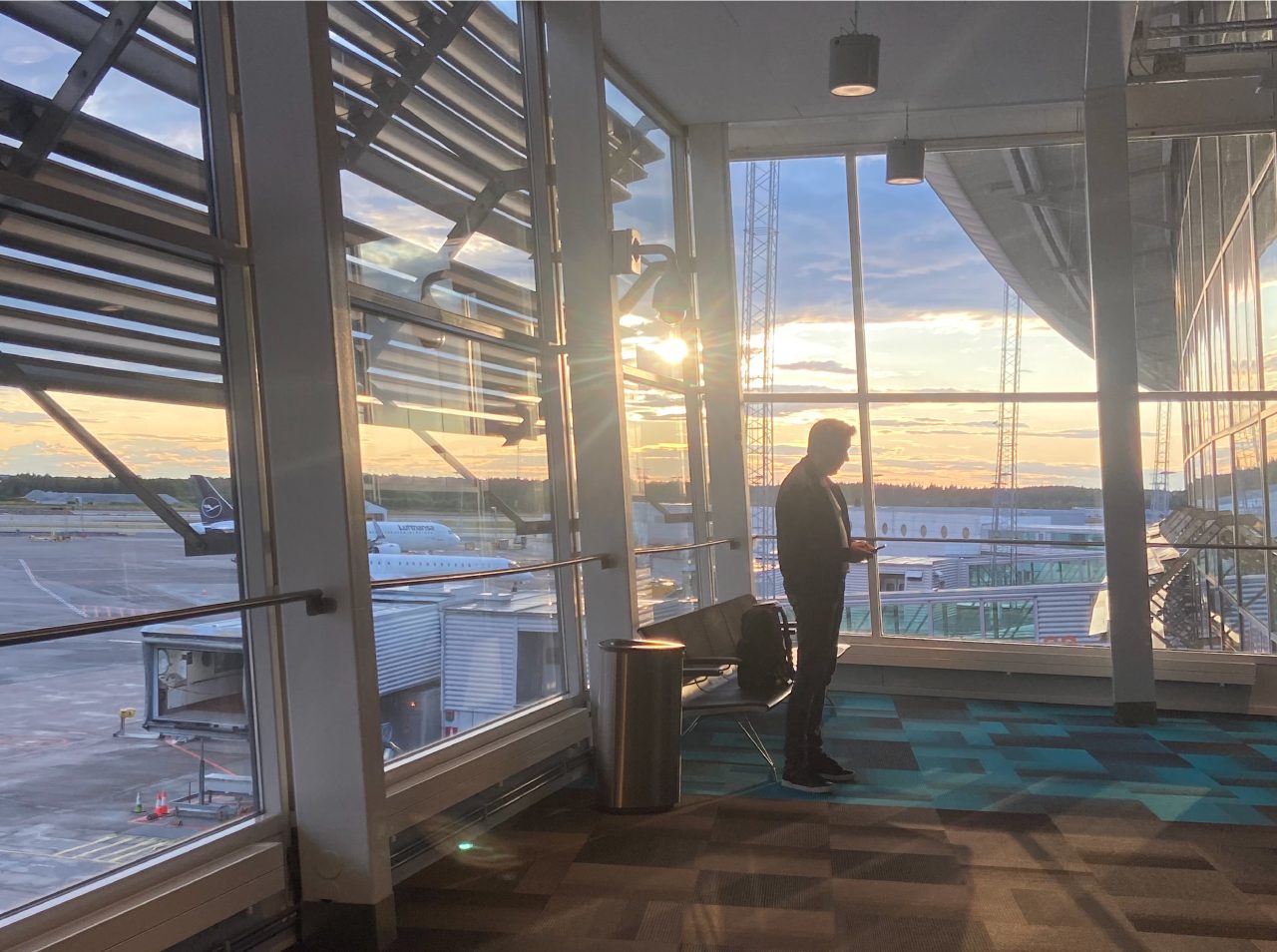 Resenär i en flygplatsterminal med flygplan utanför fönstren i kvällsljus.